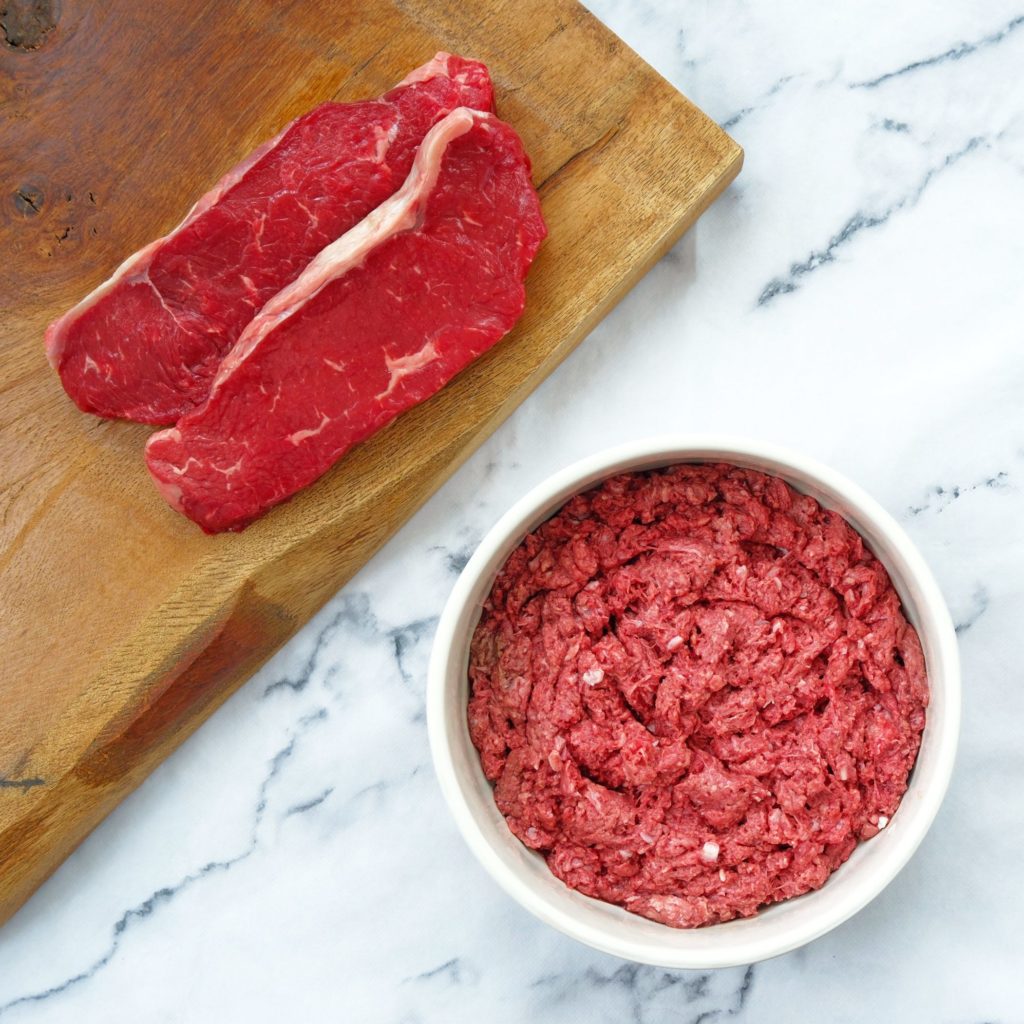 Beef mince in a dog bowl with beef steaks on a chopping board