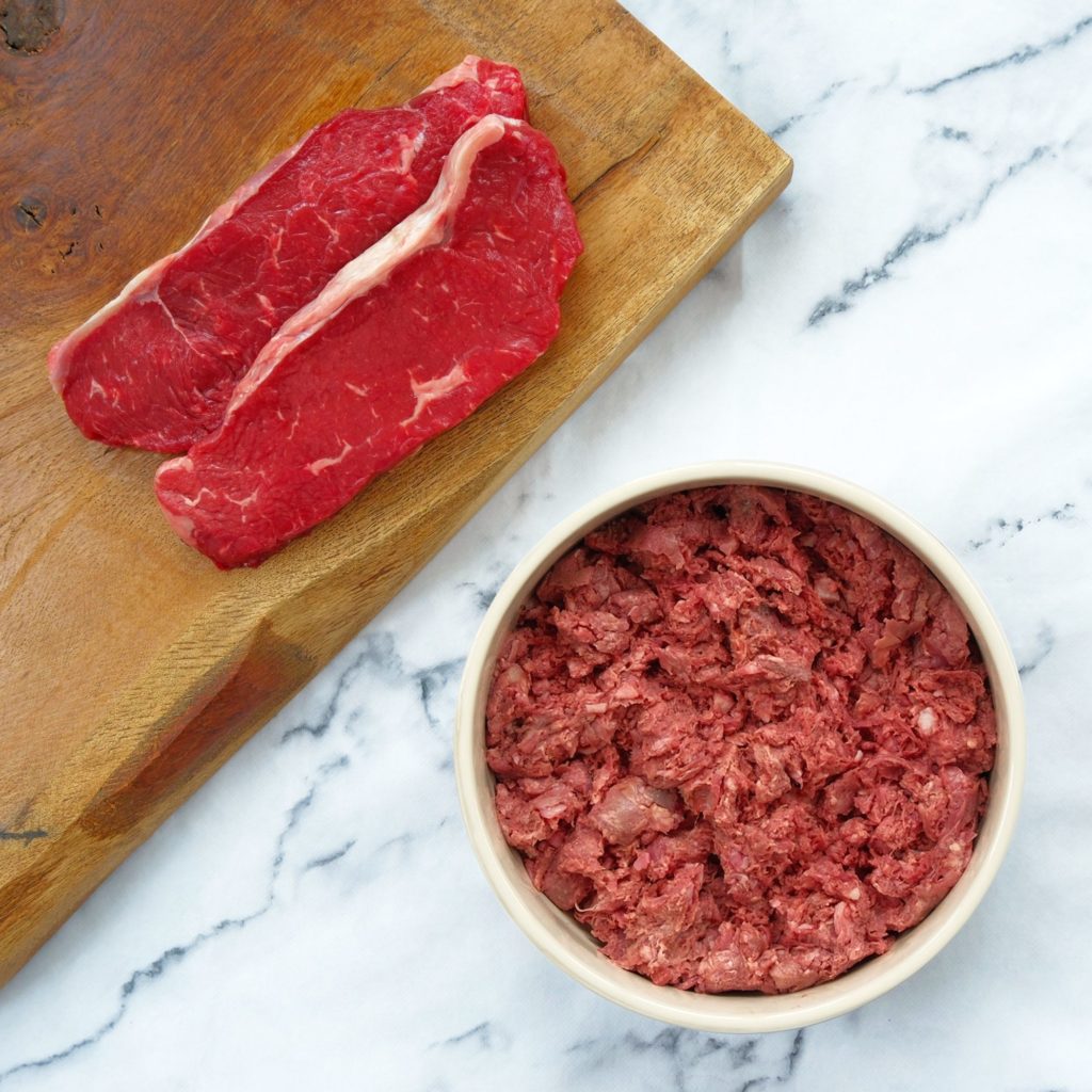 Beef and tripe mince in a dog bowl with beef steaks on a chopping board