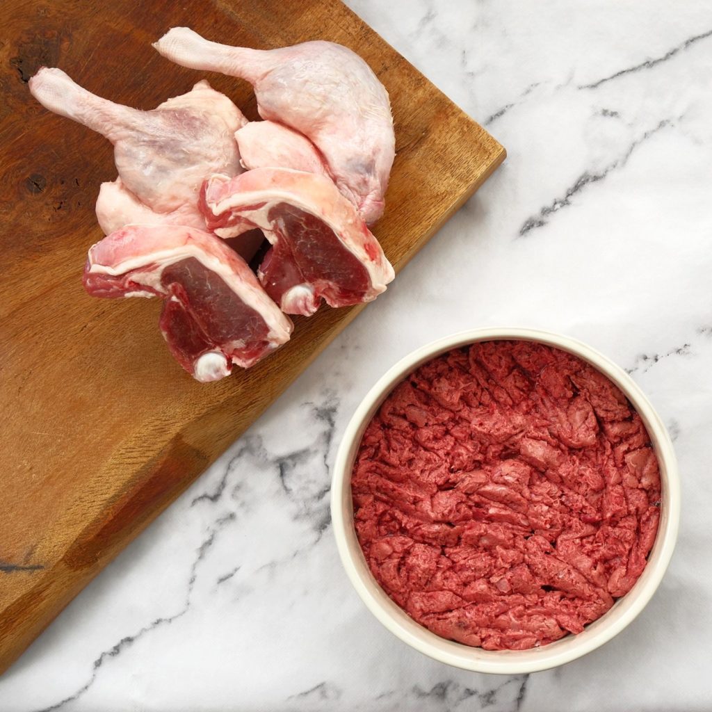 Duck and lamb mince in a dog bowl with lamb chops and duck legs on a chopping board