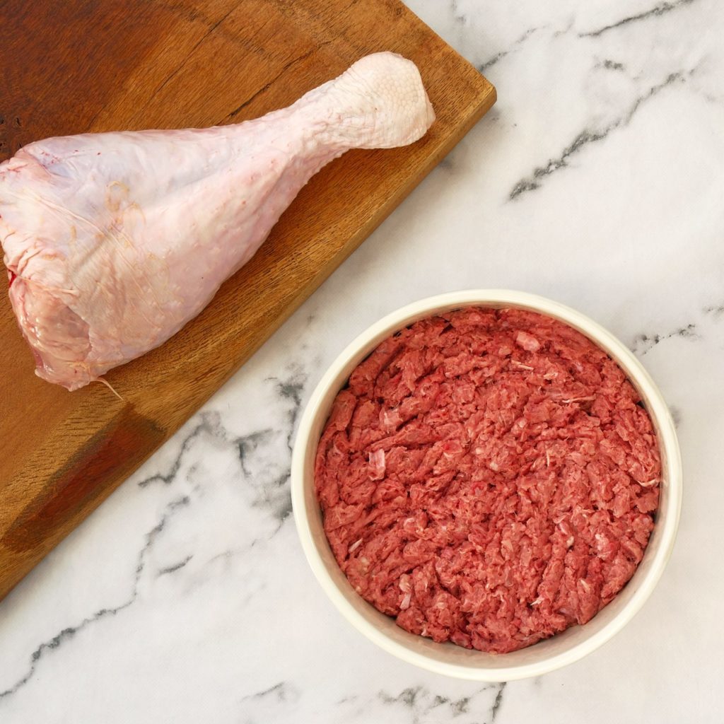 Turkey mince in a dog bowl with a turkey leg on a chopping board